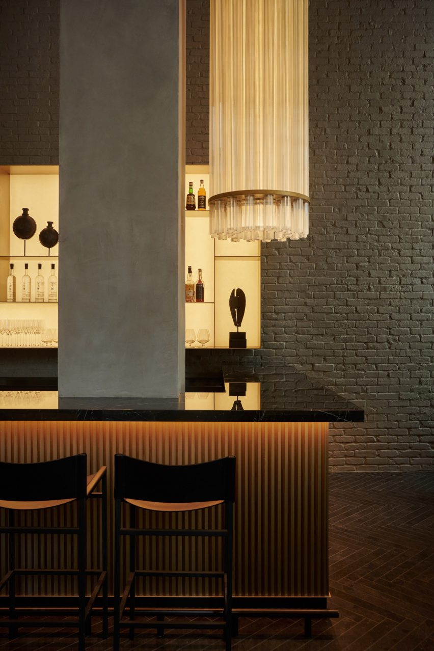 Bar with glossy black counter and fluted front, with a tall glass light fixture suspended above