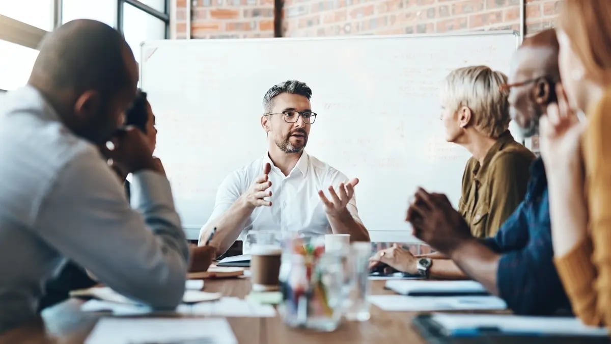 A group of colleagues discussing a strategy at a table in front of a whiteboard.