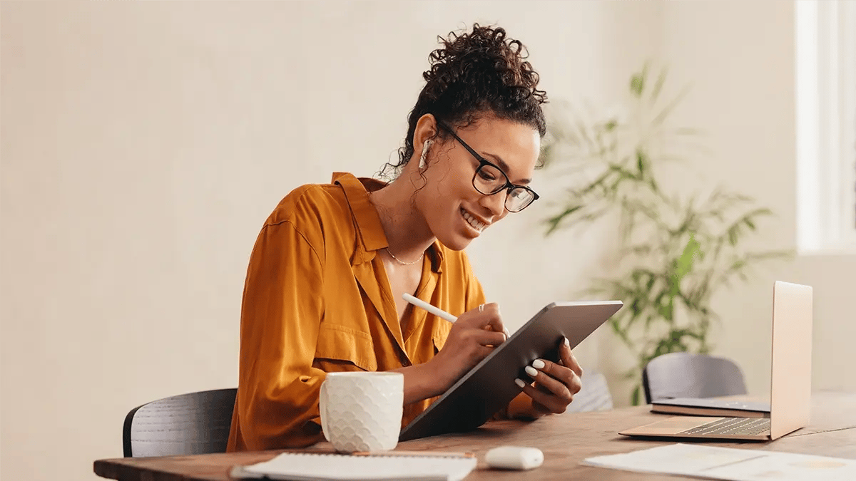 A woman in a yellow blouse holding an iPad and writing with a smart pen.