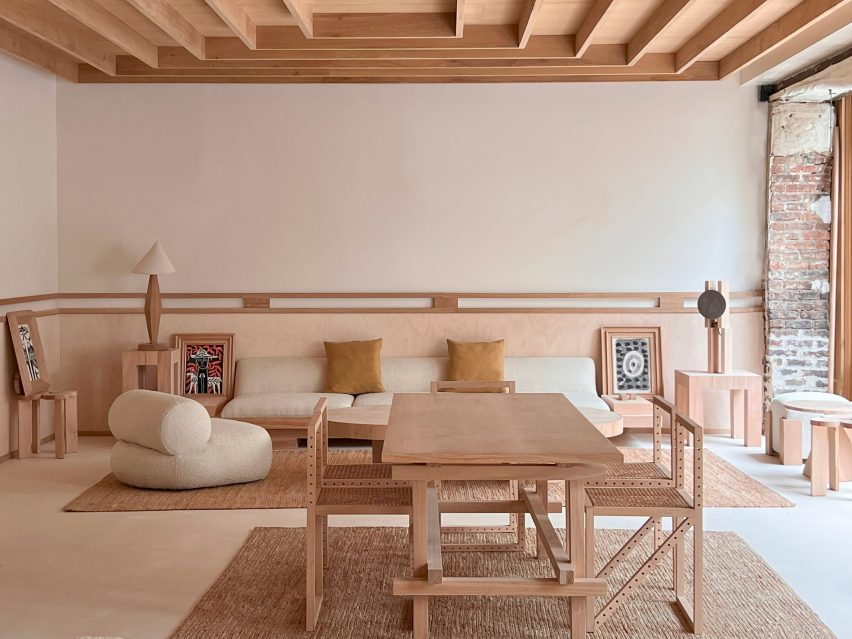 Photograph of an open plan, minimalist lounge area with a dining table. The furnishings are mostly crafted from a light toned wood.