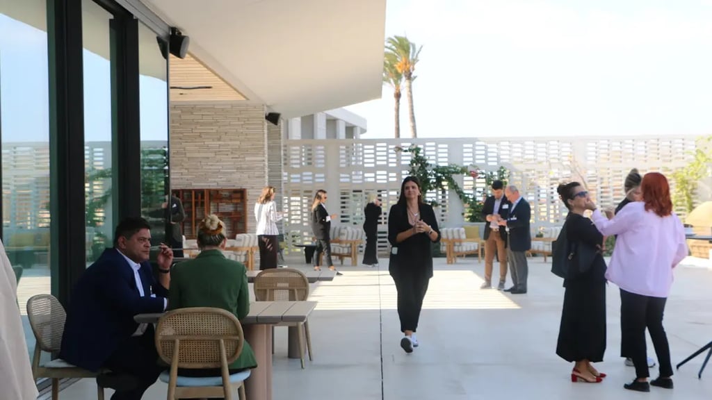 People chatting at the terrace of a white hotel with some palms in the background.