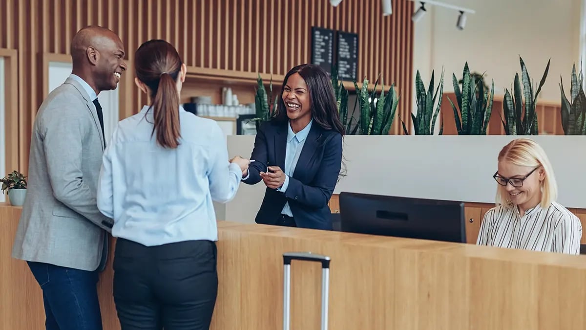 Two people checking in at a hotel desk, speaking to a concierge and smiling.