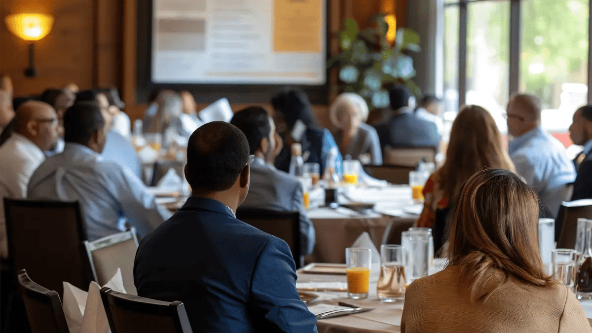 Multiple people seating at round tables at a venue looking at a presentation.