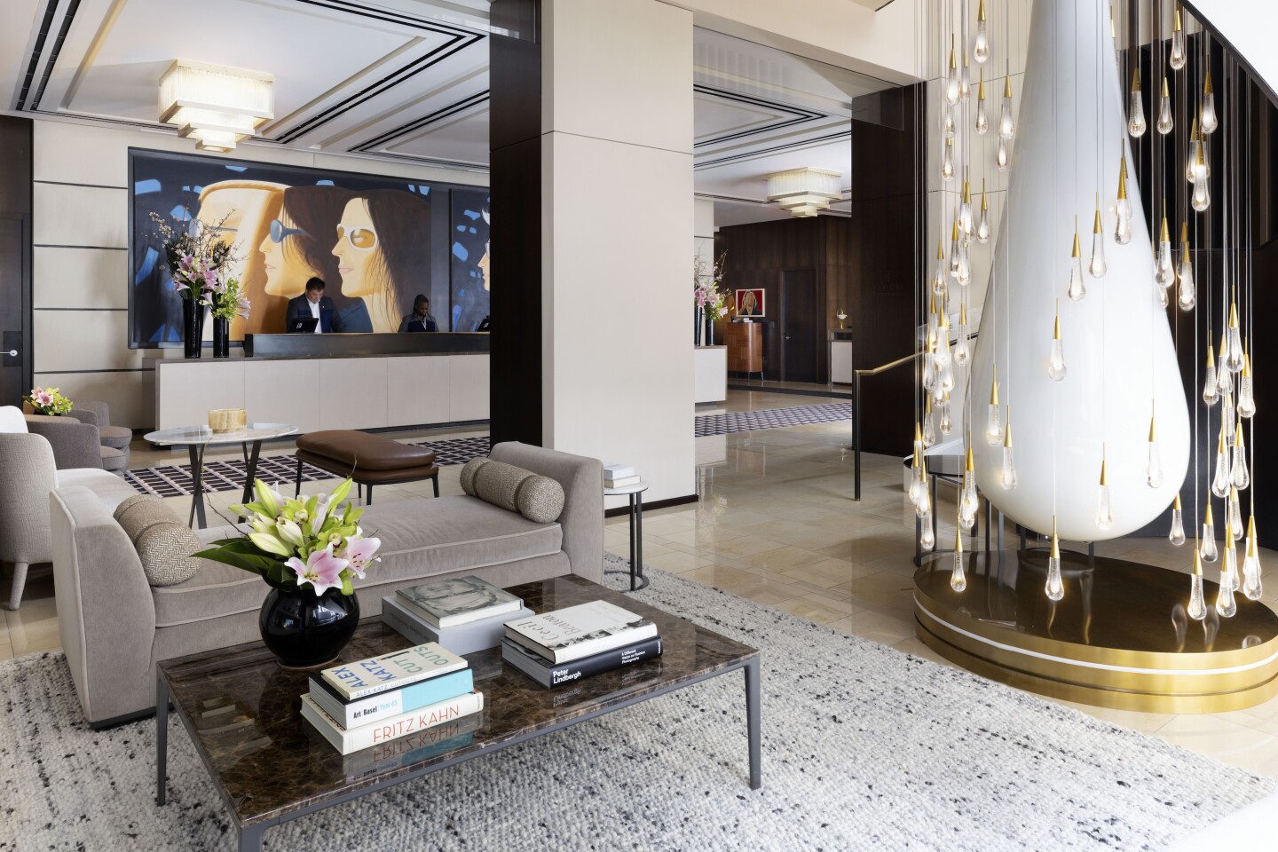 The lobby of The Langham, Fifth Avenue in New York City has paintings of American artist Alex Katz on its walls, gray and white decor, and a large white teardrop sculpture and chandelier