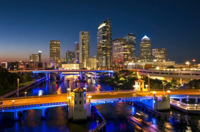 AdobeStock_1288897351-Tampa-stock Tampa city in Florida with brightly illuminated highway traffic on bridge and skyscraper buildings in downtown district. American megapolis with business financial district at night Tampa stock