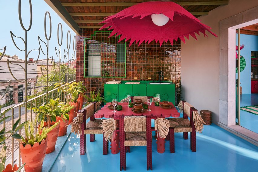 A large covered terrace with a dining table, chairs and a pink lampshade overhead