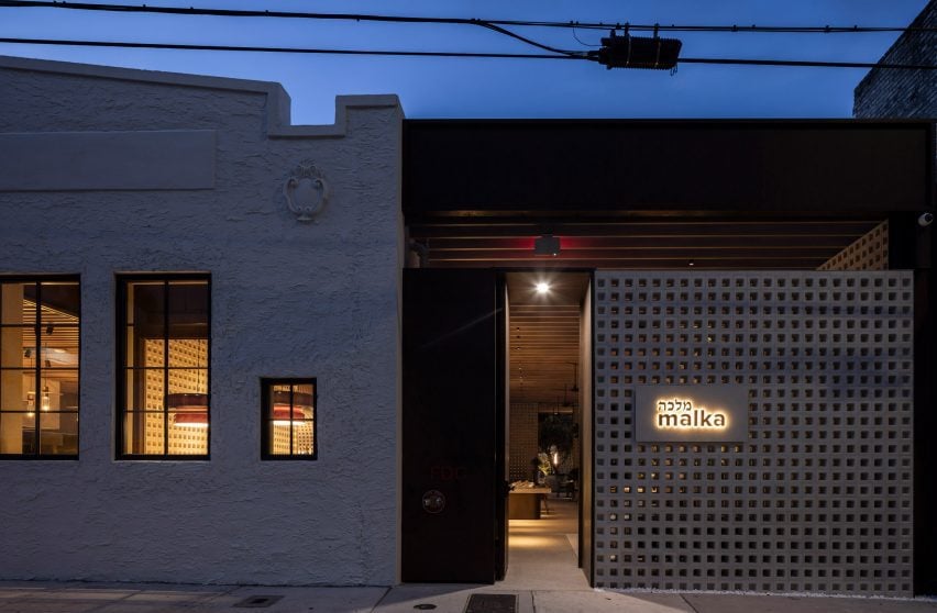 Exterior view of a 1930s building with a new perforated block wall marking the entrance