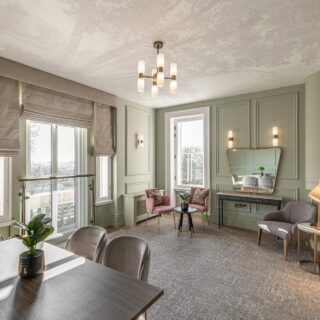 Elegant living room with sage-green paneled walls, large windows, and a modern chandelier.