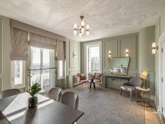 Elegant living room with sage-green paneled walls, large windows, and a modern chandelier.