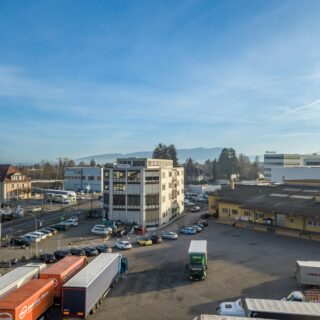 Aerial view of a logistics hub with parked trucks and a row of office buildings under a clear blue sky.