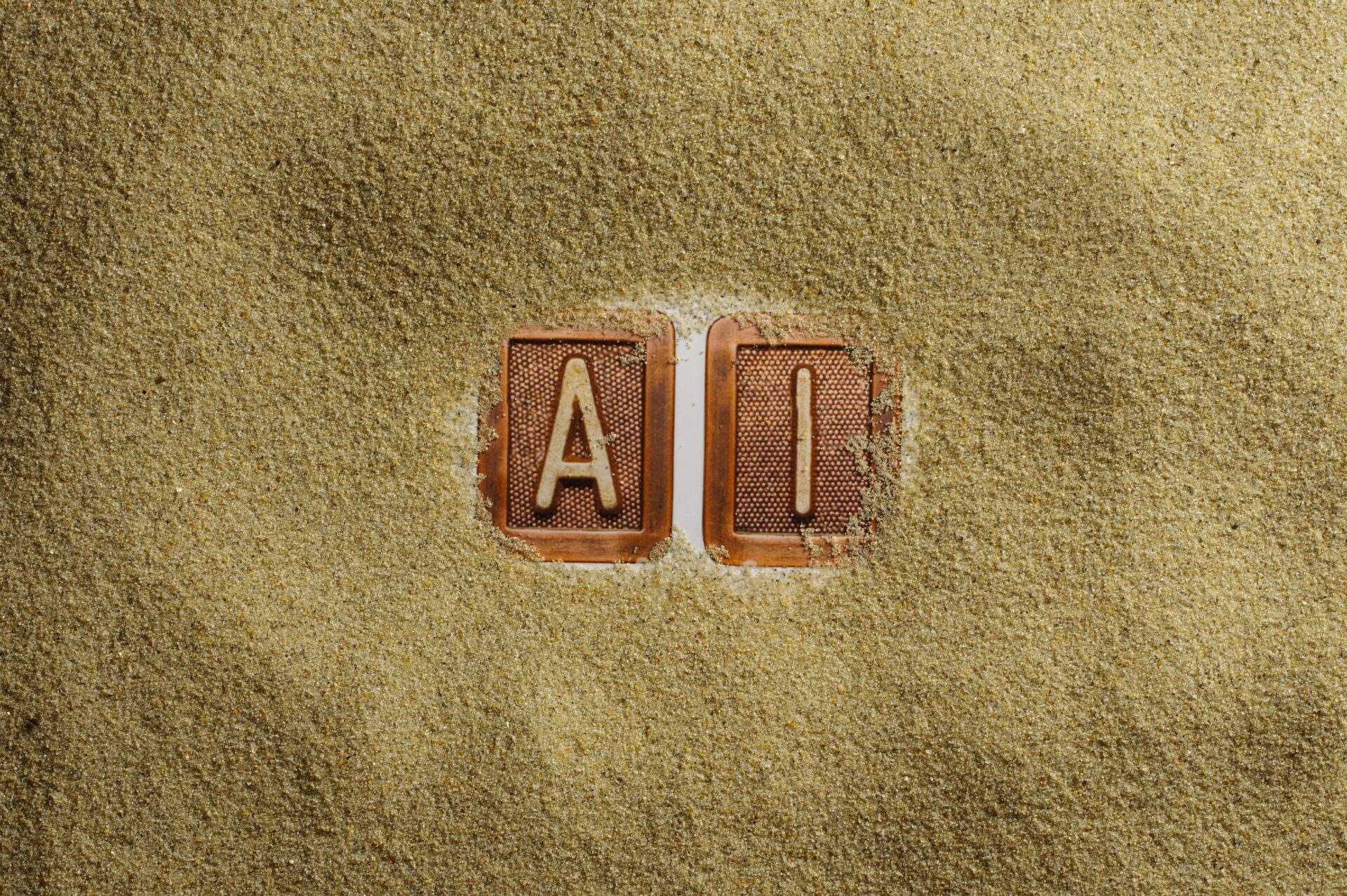 Two clay tiles with the letters A and I, partly buried in coarse sand.