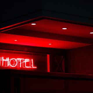 Red neon letters spelling HOTEL glow in a dark building entrance at night.