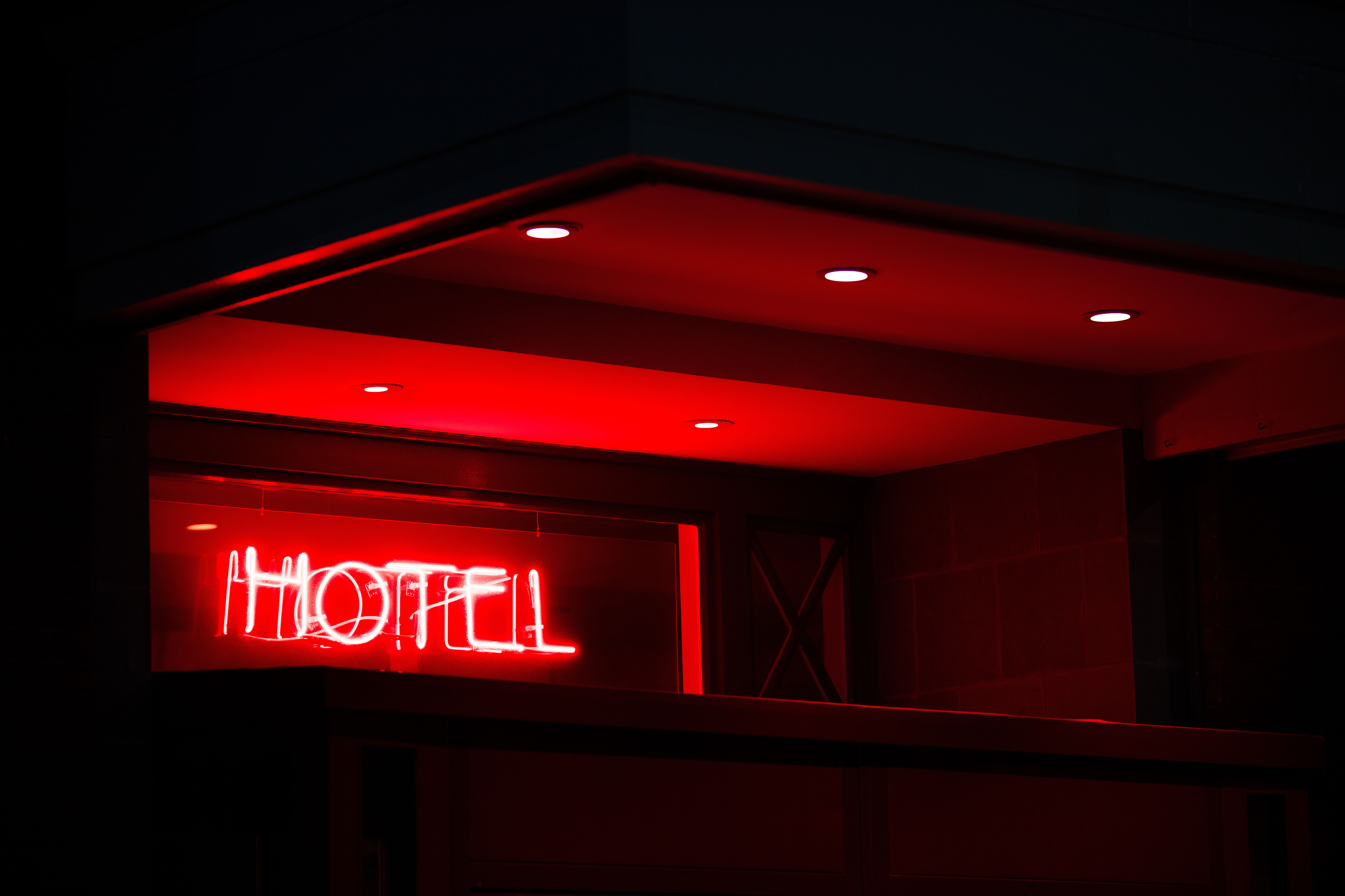 Red neon letters spelling HOTEL glow in a dark building entrance at night.