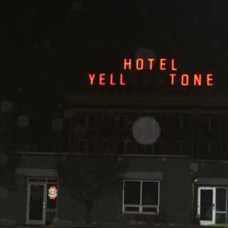 Night exterior of a building with a red neon sign reading 'HOTEL YELL TONE' on the roof, illuminated against a dark sky.