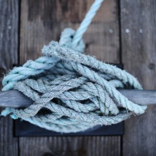 Close-up of frayed blue-green rope coiled on weathered wooden dock planks.