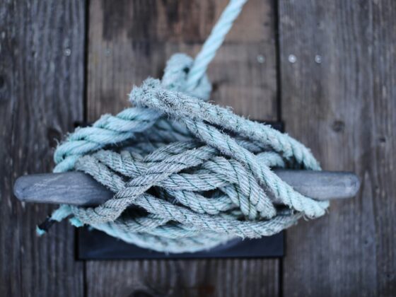Close-up of frayed blue-green rope coiled on weathered wooden dock planks.