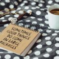 Notebook on a polka-dot blanket with the phrase “Sometimes good things come in large packages,” beside a cup of tea with a lemon slice and glasses nearby.