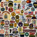 A colorful collage of embroidered patches and badges from schools, clubs, and organizations on a white wall.