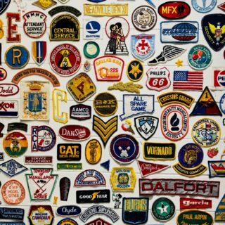 A colorful collage of embroidered patches and badges from schools, clubs, and organizations on a white wall.