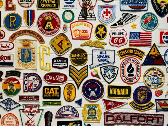 A colorful collage of embroidered patches and badges from schools, clubs, and organizations on a white wall.