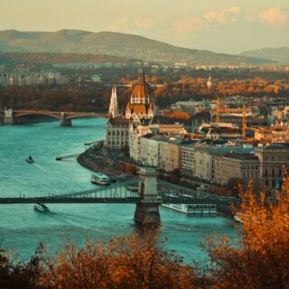 Wide view of Budapest with the Danube River, Chain Bridge, and the Parliament Building along the riverfront during autumn.