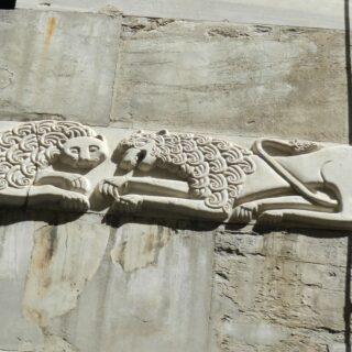 Decorative stone relief showing two lions with curly manes lying on a weathered wall edge.