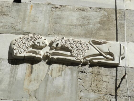 Decorative stone relief showing two lions with curly manes lying on a weathered wall edge.