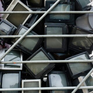 Pile of old CRT televisions and computer monitors squeezed together behind metal scaffolding.