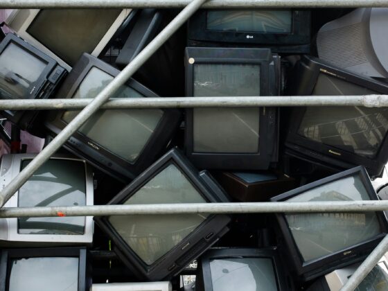 Pile of old CRT televisions and computer monitors squeezed together behind metal scaffolding.