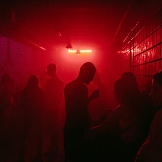 Dim red-lit club corridor with silhouetted people standing and talking.