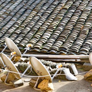 Row of white satellite dishes facing various directions on a tiled rooftop, with rubble and debris around them.