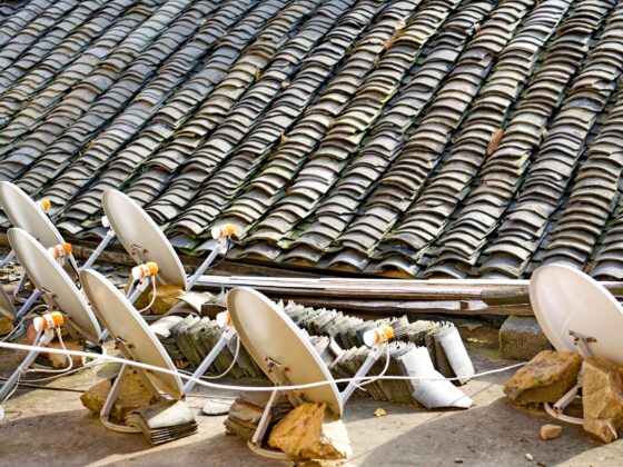 Row of white satellite dishes facing various directions on a tiled rooftop, with rubble and debris around them.