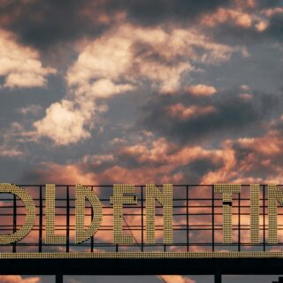 Backlit sign reading 'GOLDEN TIME' with illuminated bulbs against a sunset sky.