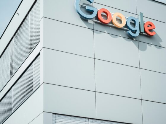 Colorful Google letters mounted on the exterior wall of a modern gray office building against a blue sky.