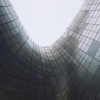 Curved silver building exterior with grid-pattern metal panels forming an open space between towers.