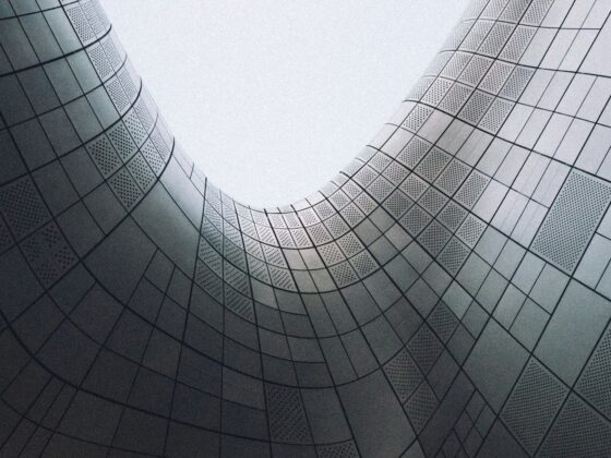 Curved silver building exterior with grid-pattern metal panels forming an open space between towers.