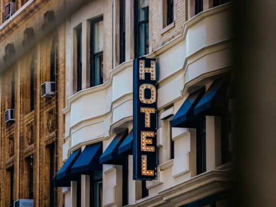 Historic brick building with a vertical lit hotel sign and blue awnings outside.