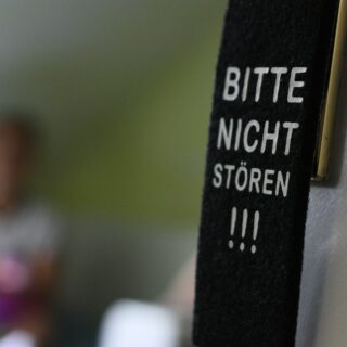 Door hanger with the German phrase 'BITTE NICHT STÖREN' visible on a dark strap attached to a wall.