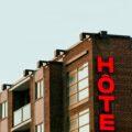 Corner of a brick building with a vertical red 'HOTEL' sign along the facade.