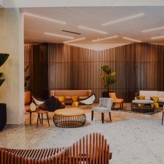 Modern hotel lobby lounge with curved wooden slat partitions, potted plants, and beige seating.