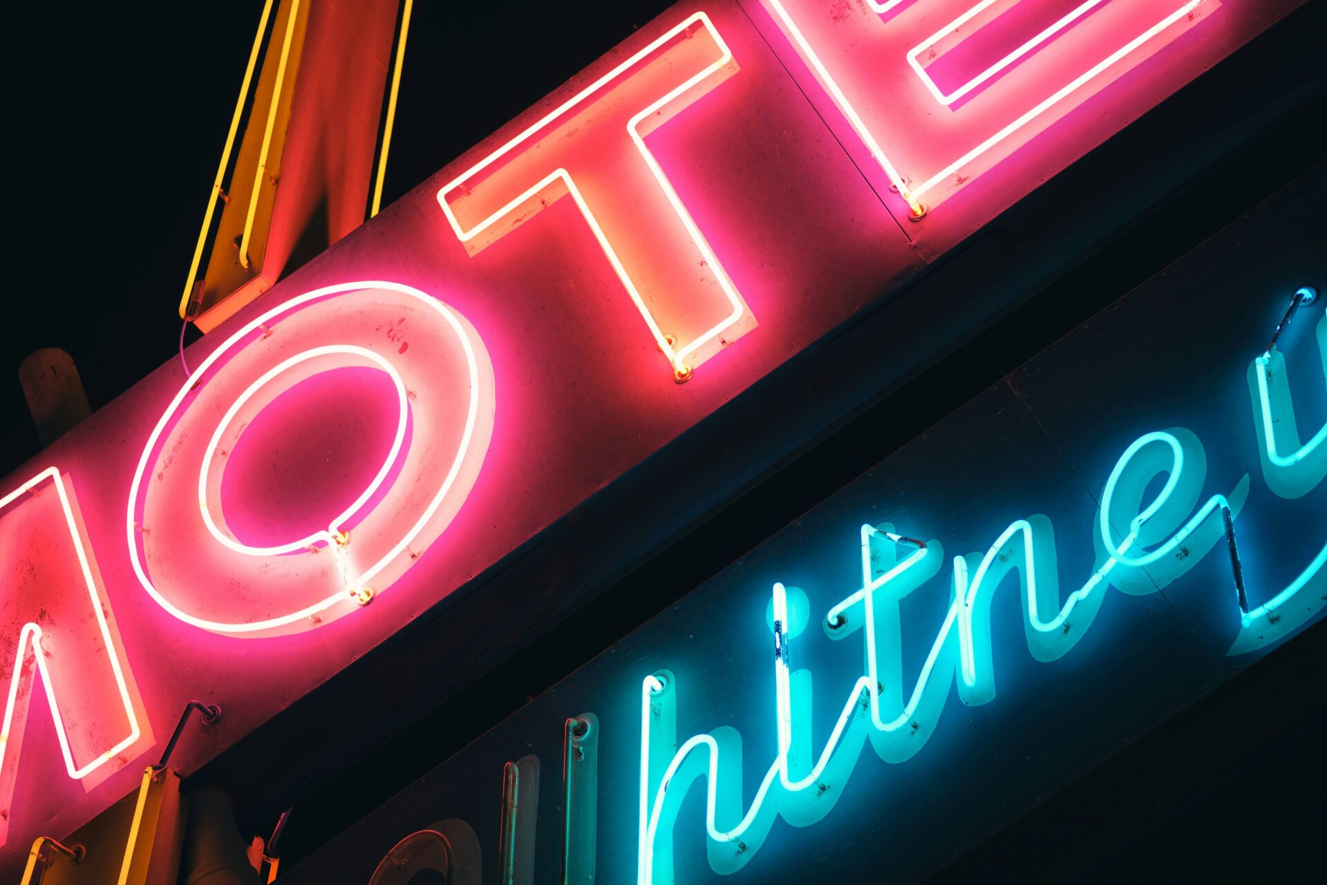 Close-up of a pink and blue neon sign glowing against a dark storefront edge at night.