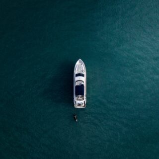 Aerial view of a white motor yacht on dark turquoise water with a small tender nearby below the stern.
