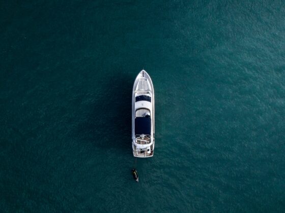 Aerial view of a white motor yacht on dark turquoise water with a small tender nearby below the stern.