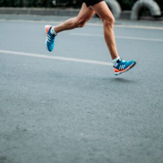 A runner's legs in mid-stride on a track, wearing blue and orange athletic shoes with white socks.