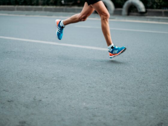 A runner's legs in mid-stride on a track, wearing blue and orange athletic shoes with white socks.
