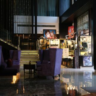 Luxurious hotel lobby with glass jewelry displays, purple velvet chairs, and a marble floor reflected in the surface.
