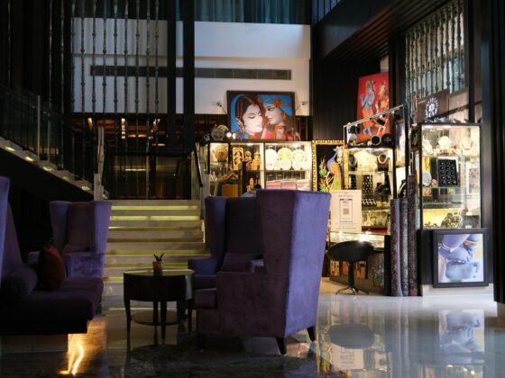 Luxurious hotel lobby with glass jewelry displays, purple velvet chairs, and a marble floor reflected in the surface.