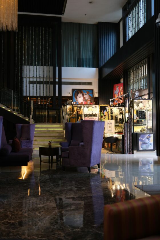 Luxurious hotel lobby with glass jewelry displays, purple velvet chairs, and a marble floor reflected in the surface.