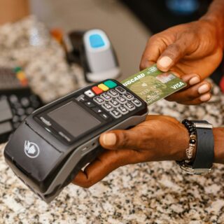 Close-up of a hand holding a green Visa credit card over a payment terminal, ready to pay on a granite countertop.
