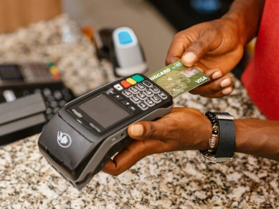 Close-up of a hand holding a green Visa credit card over a payment terminal, ready to pay on a granite countertop.